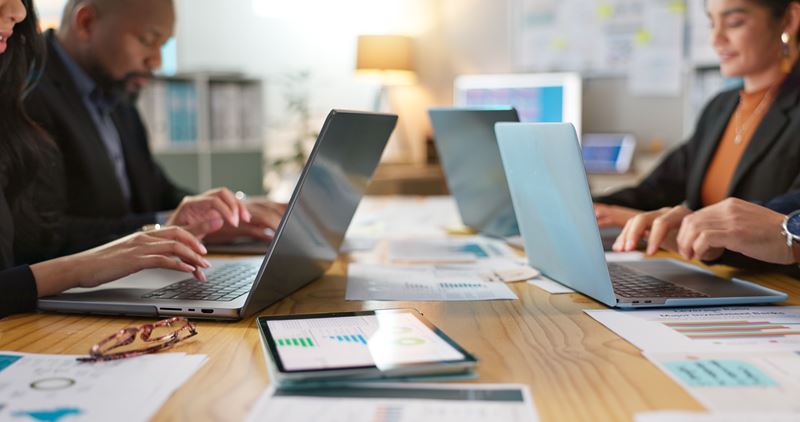 A close up of a boardroom table with several people working on laptops.